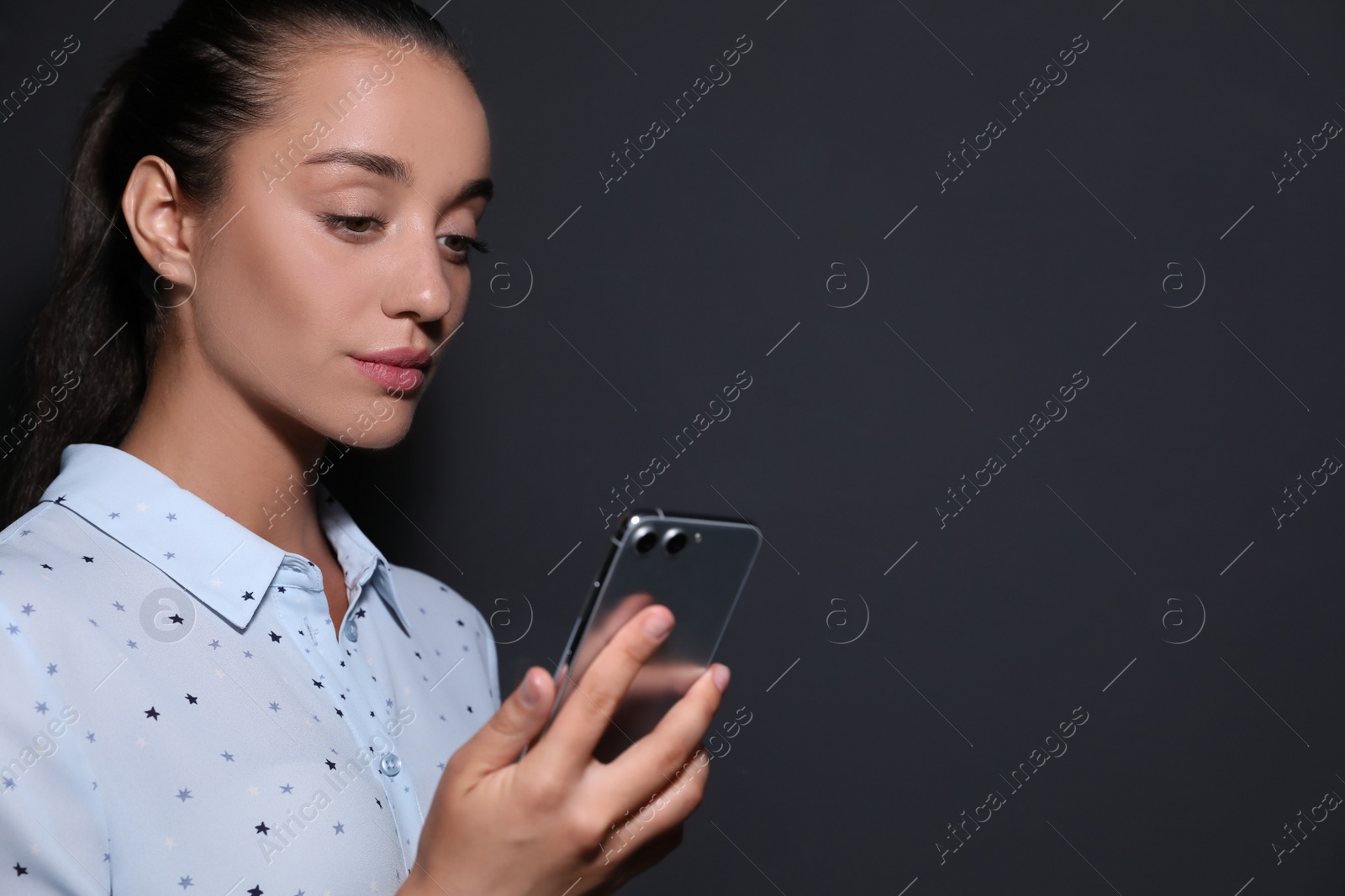 Photo of Young woman unlocking smartphone with facial scanner on black background, space for text. Biometric verification