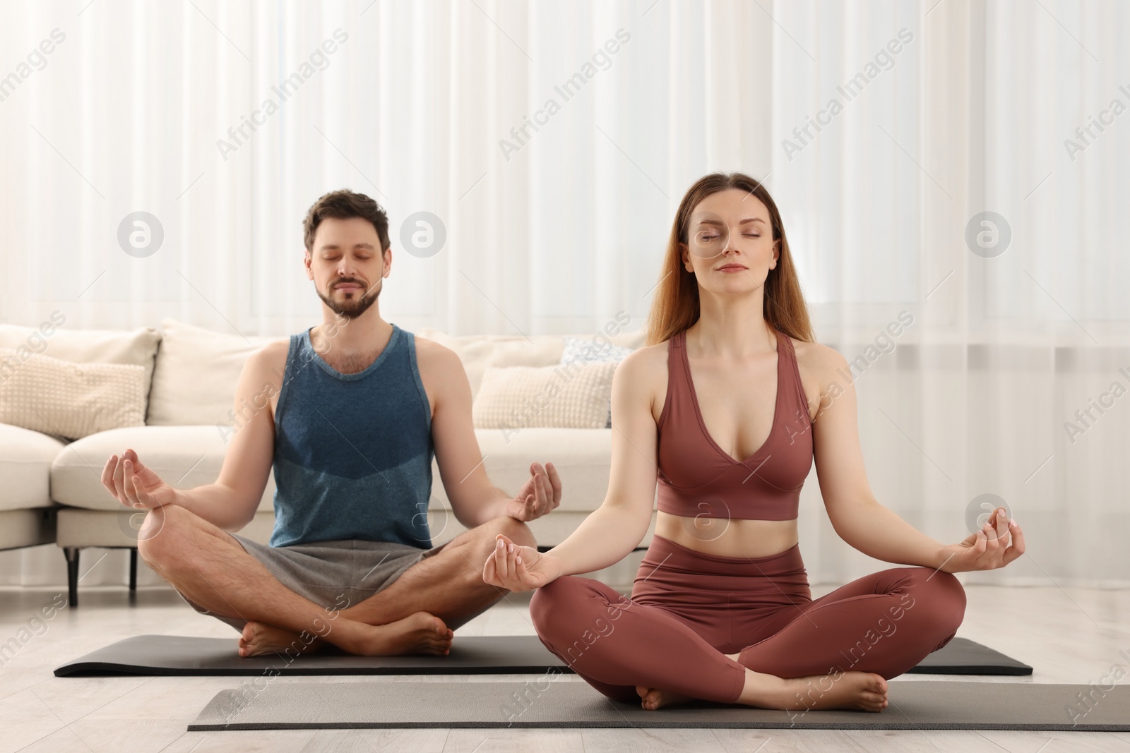 Photo of Couple in sportswear meditating together at home. Harmony and zen