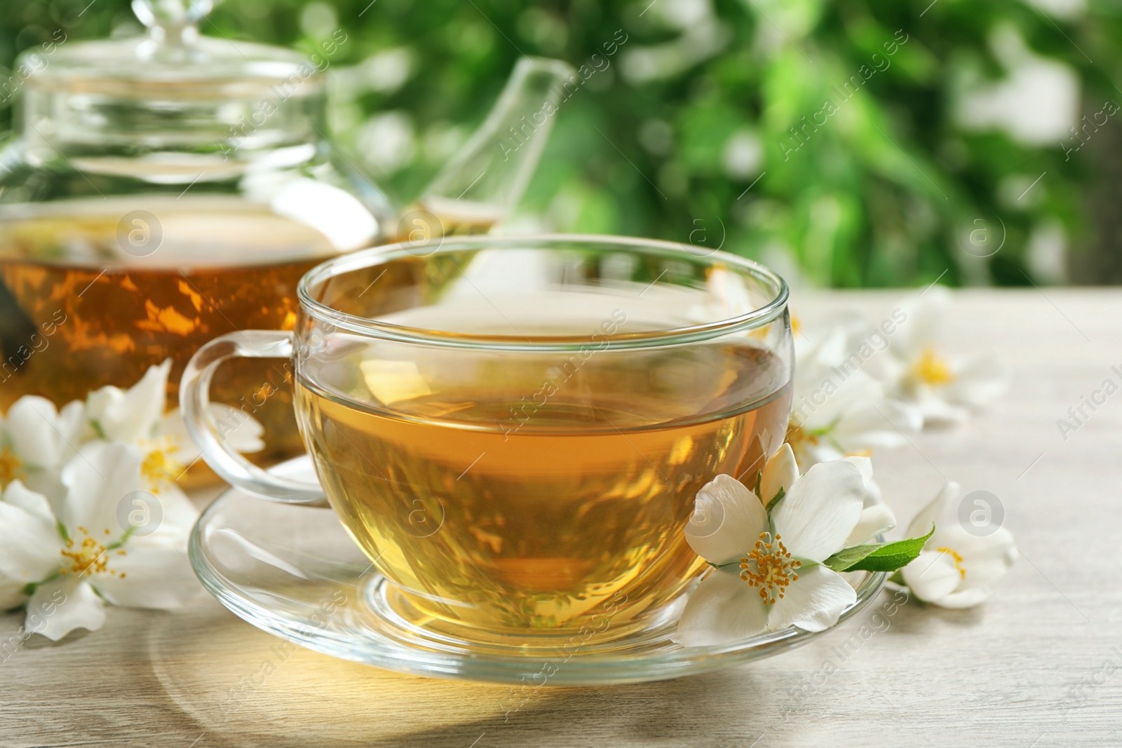 Photo of Aromatic jasmine tea and fresh flowers on wooden table, closeup