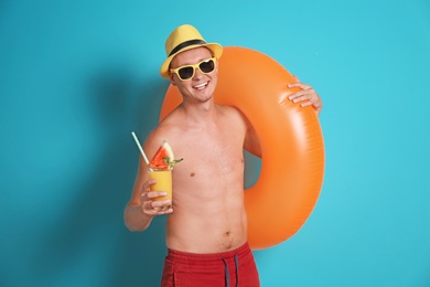 Shirtless man with inflatable ring and glass of cocktail on color background