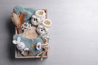 Photo of Wooden box with baby clothes, booties and accessories on grey background, top view. Space for text