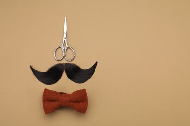 Photo of Artificial moustache, bow tie and scissors on beige background, top view. Space for text