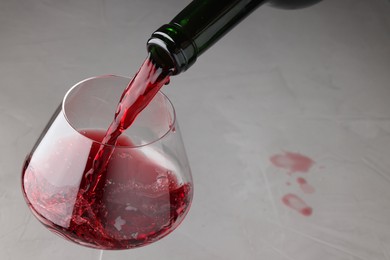 Pouring tasty red wine in glass at gray table, closeup. Space for text