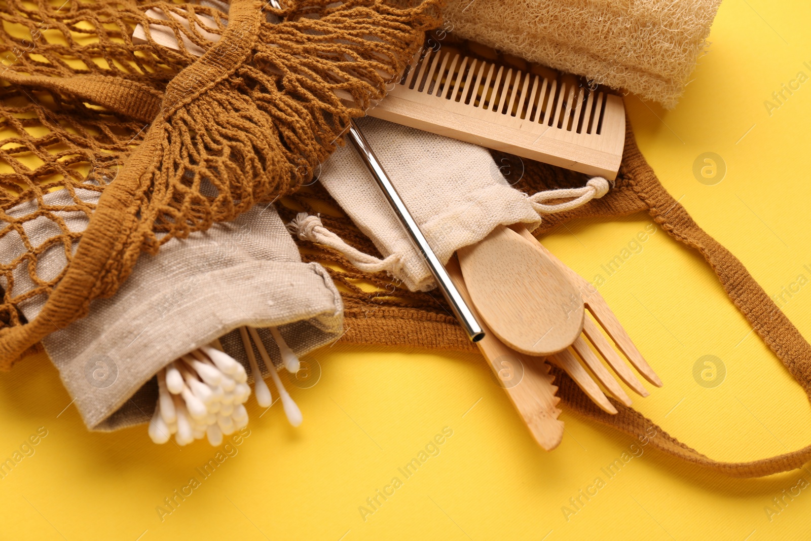 Photo of Fishnet bag with different items on yellow background, closeup. Conscious consumption