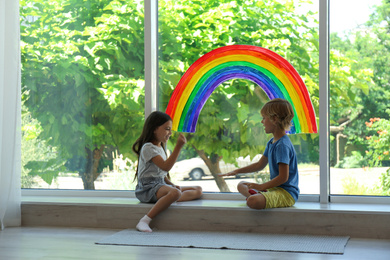 Little children playing near rainbow painting on window indoors. Stay at home concept