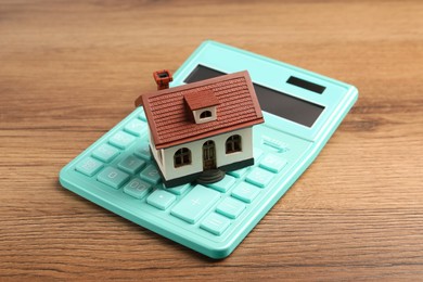 Photo of Mortgage concept. House model and calculator on wooden table, closeup