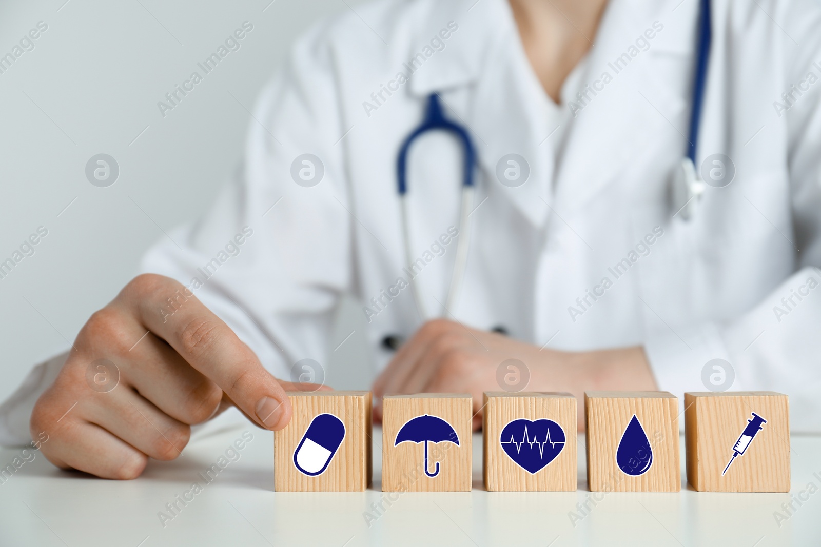 Image of Doctor and wooden cubes with different icons on white table, closeup. Insurance concept