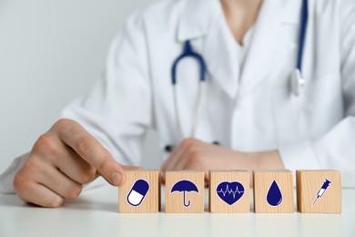 Doctor and wooden cubes with different icons on white table, closeup. Insurance concept