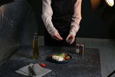 Photo of Food stylist preparing delicious salad with mozzarella and tomatoes for photoshoot at dark grey table in studio, closeup