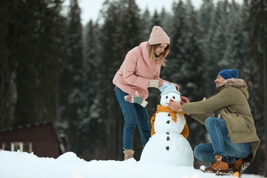 Photo of Couple making snowman near forest. Winter vacation