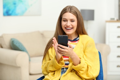 Happy young woman playing online lottery using smartphone at home