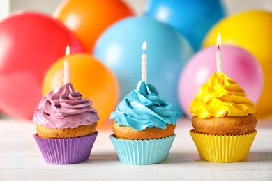Photo of Delicious birthday cupcakes with candles and blurred balloons on background