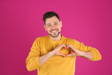 Portrait of handsome man making heart with his hands on color background