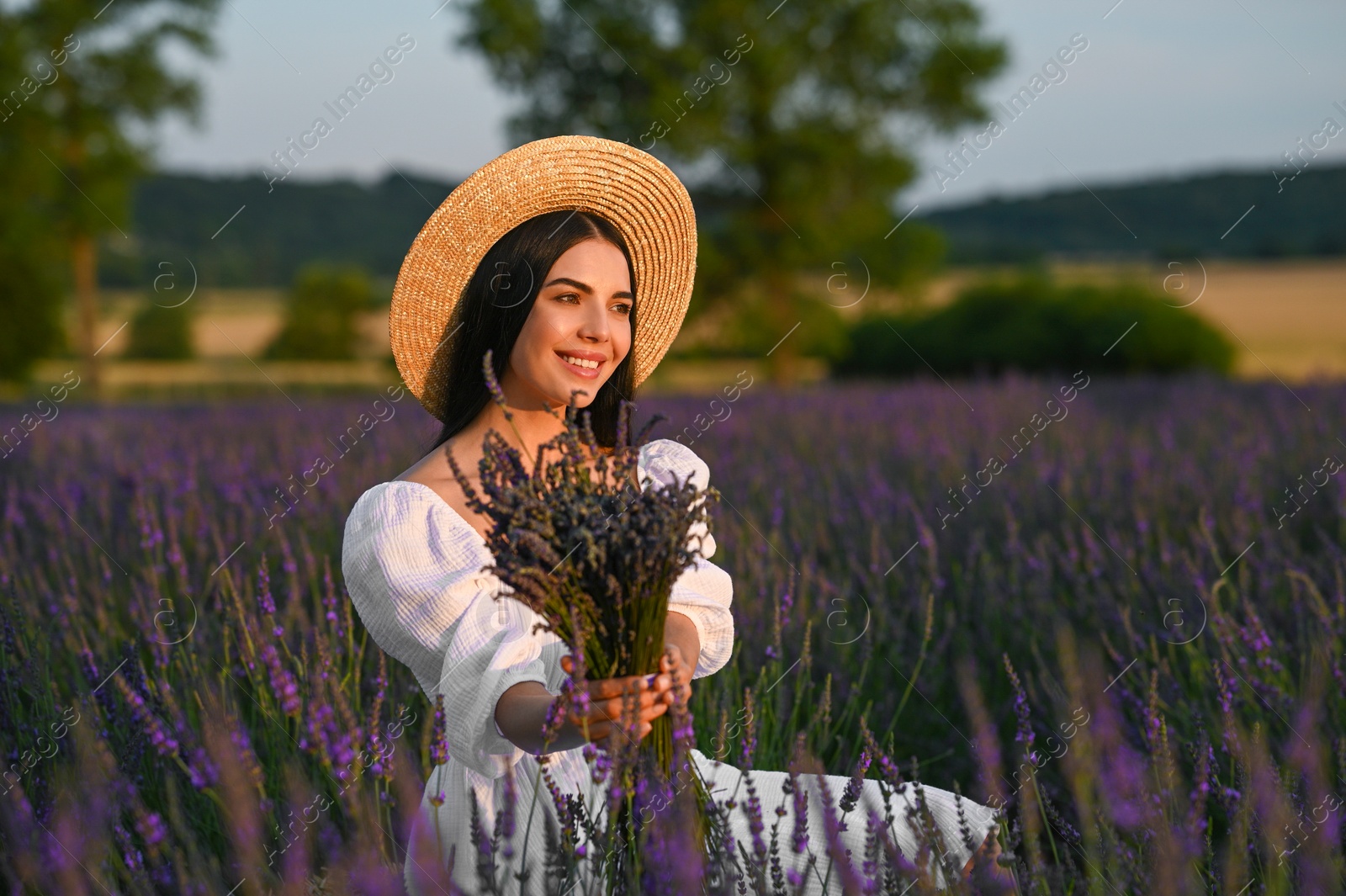 Photo of Beautiful young woman with bouquet sitting in lavender field