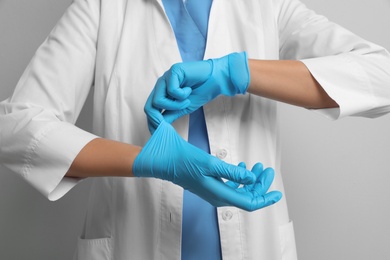 Photo of Doctor putting on medical gloves against light grey background, closeup