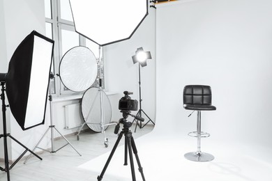 Tripod with camera, bar stool and professional lighting equipment in modern photo studio