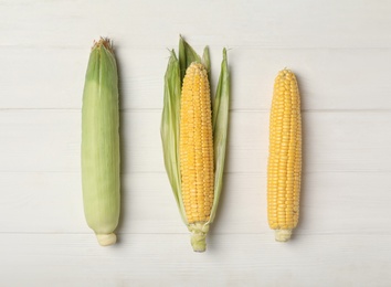 Corn cobs on white wooden table, flat lay