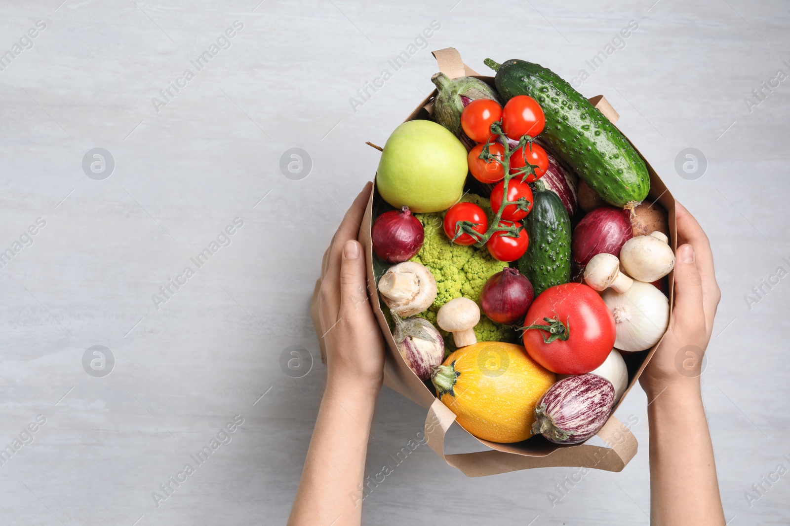 Photo of Woman holding paper bag with fresh vegetables on light background, top view. Space for text