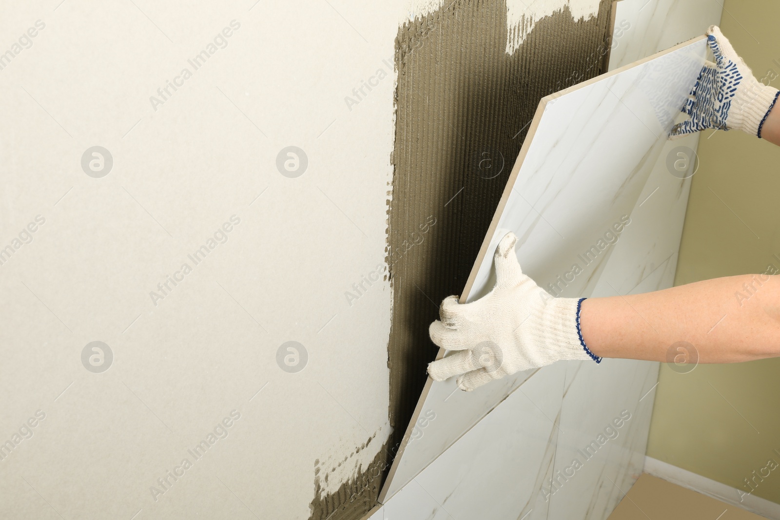 Photo of Worker installing ceramic tile on wall, closeup. Space for text