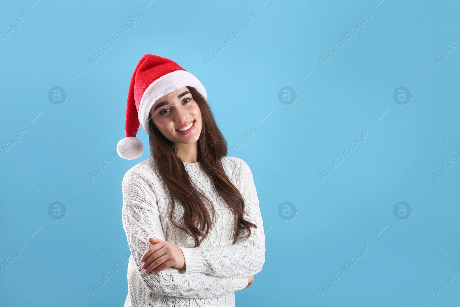 Photo of Beautiful woman wearing Santa Claus hat on light blue background. Space for text