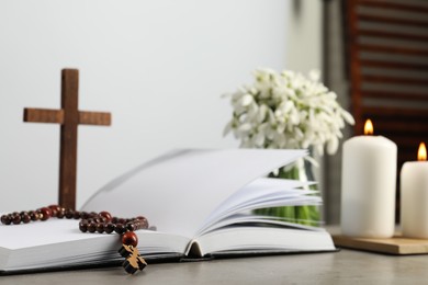 Photo of Church candles, Bible, wooden cross, rosary beads and flowers on grey table