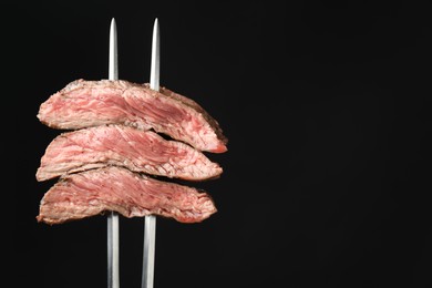 Photo of Meat fork with grilled beef pieces on black background, closeup. Space for text