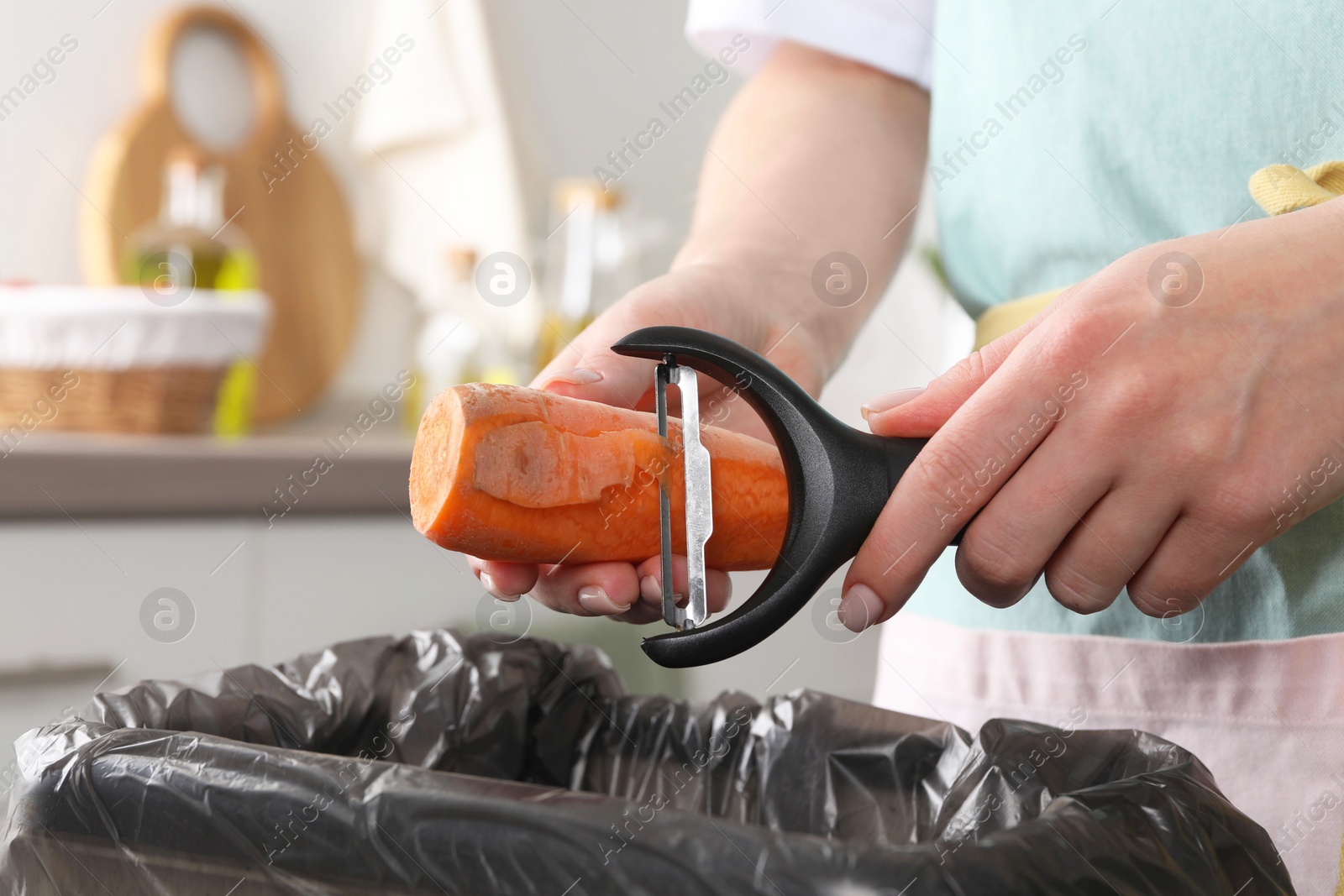 Photo of Woman peeling fresh carrot above garbage bin indoors, closeup