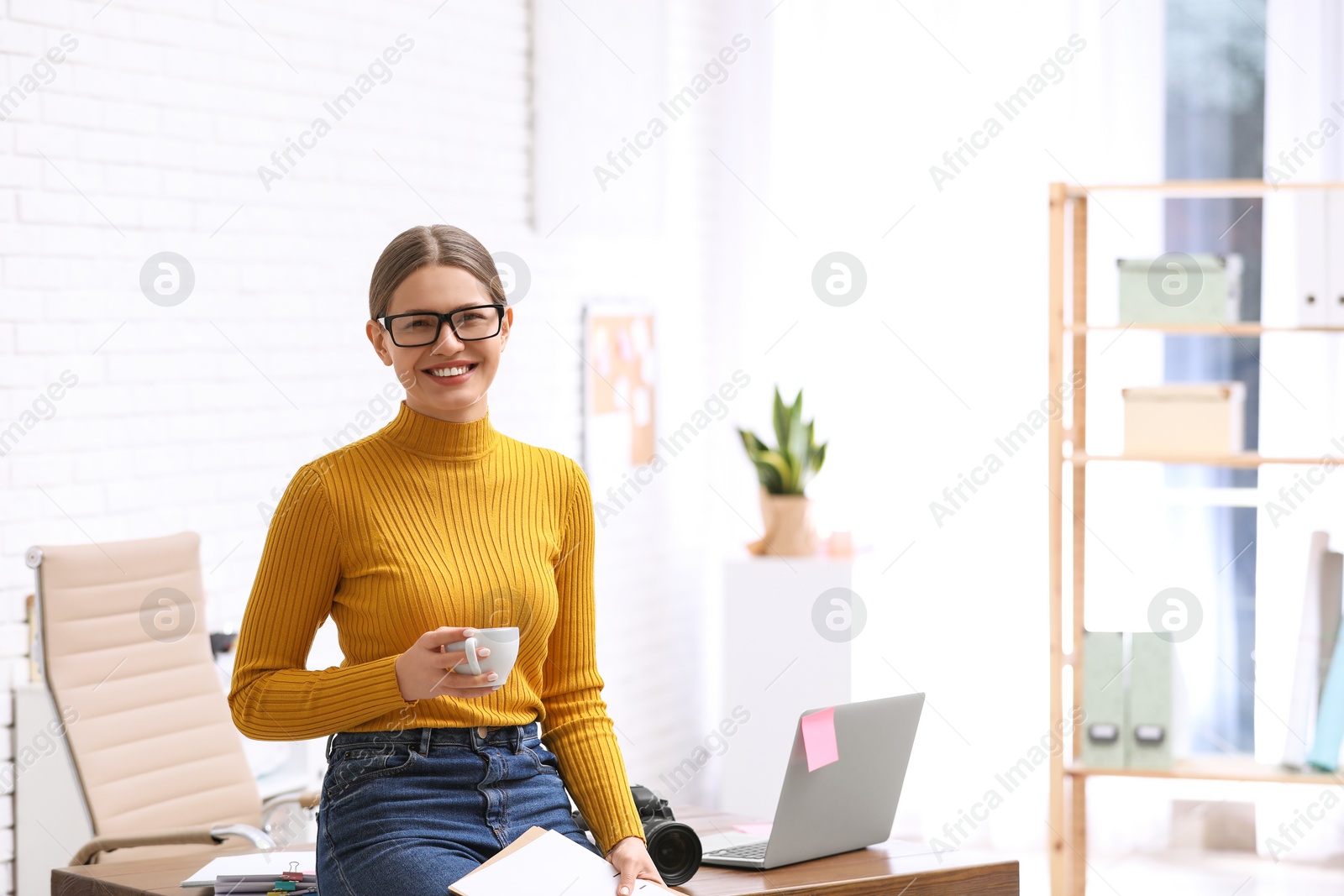 Photo of Young journalist with coffee at workplace in light office