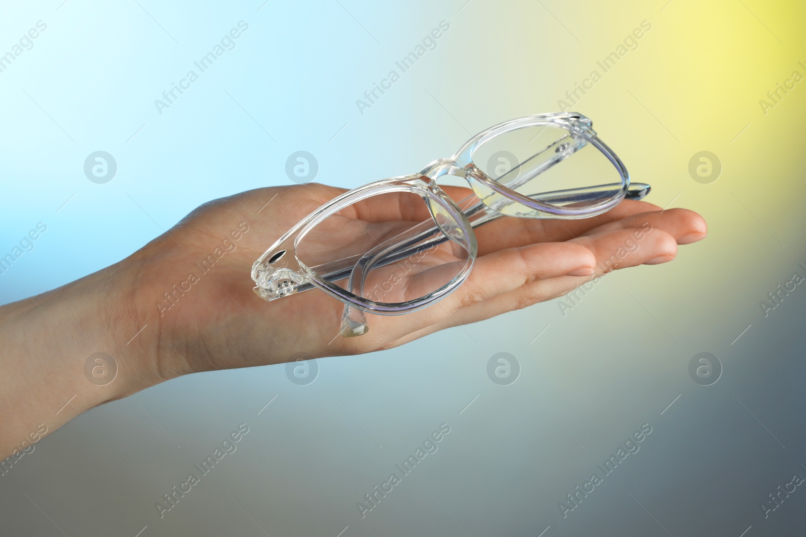 Photo of Woman holding glasses with transparent frame on color background, closeup