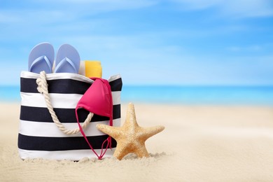 Image of Bag with bikini and accessories on sunny ocean beach, space for text. Summer vacation