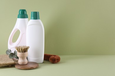 Bottles of cleaning product, sponges and brush on light green background. Space for text