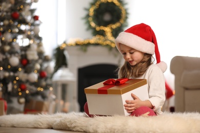 Photo of Cute little girl holding gift box in room decorated for Christmas