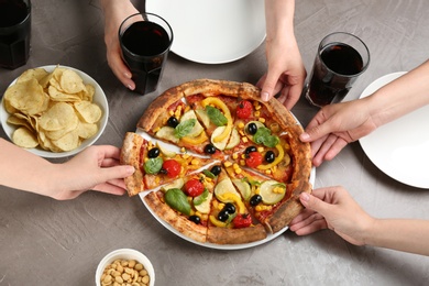 Photo of Women taking slices of delicious vegetable pizza at grey table, closeup