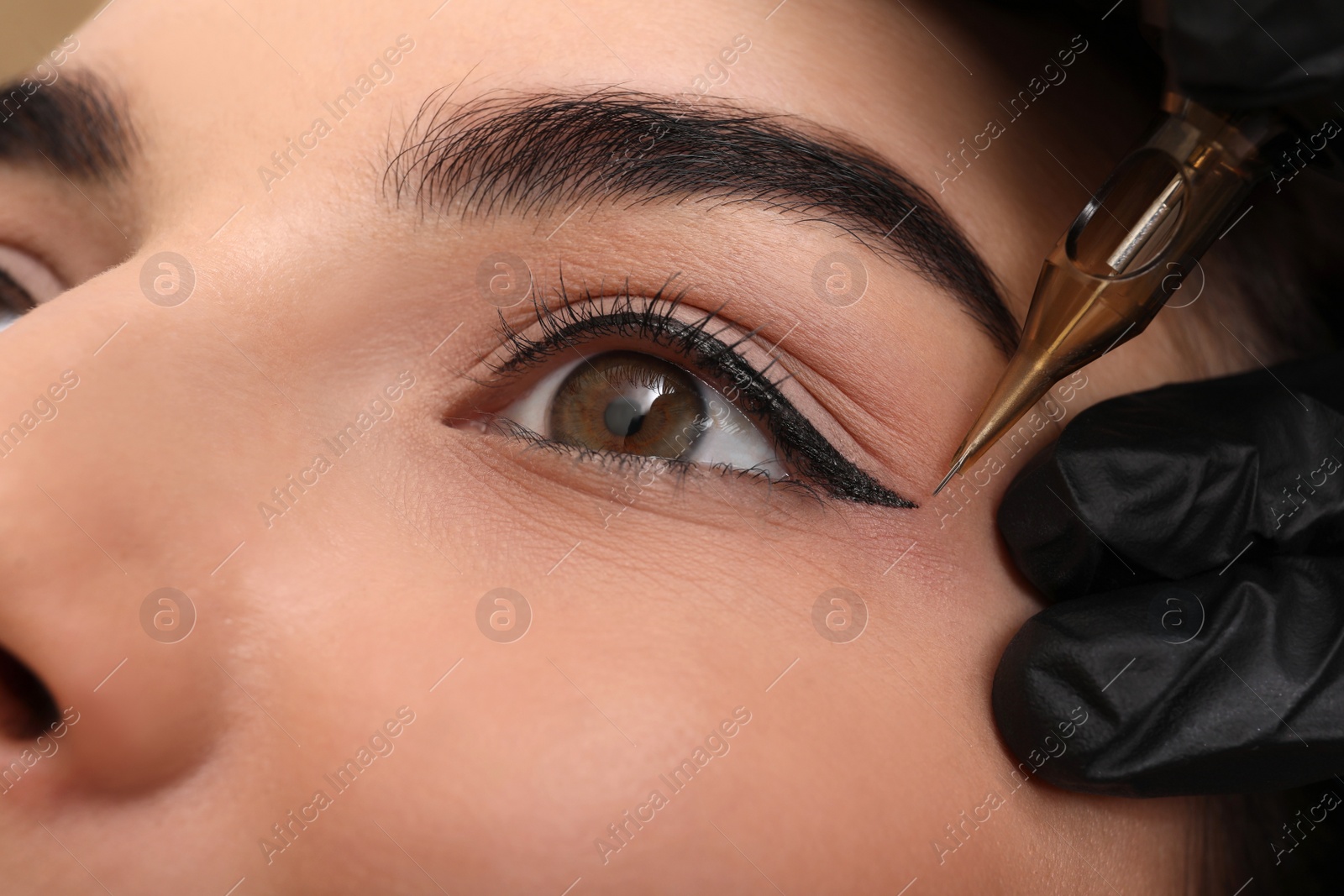 Photo of Young woman undergoing procedure of permanent eye makeup in tattoo salon, closeup