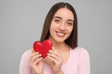 Happy young woman holding decorative red heart on light grey background