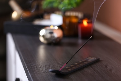 Incense stick smoldering on wooden chest of drawers in room. Space for text