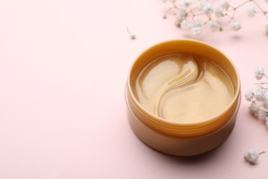 Photo of Under eye patches in jar and flowers on light pink background, space for text. Cosmetic product