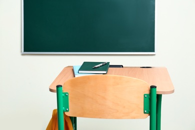 School desk with stationery and bag near chalkboard in classroom