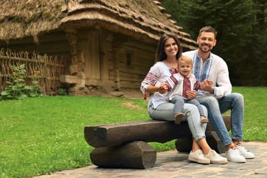 Photo of Happy family in Ukrainian national clothes sitting on bench outdoors