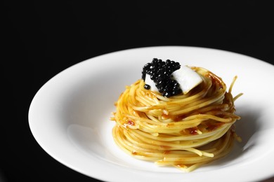 Photo of Tasty spaghetti with tomato sauce and black caviar on dark background, closeup. Exquisite presentation of pasta dish