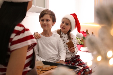 Mother giving her cute little children freshly baked Christmas cookies in kitchen