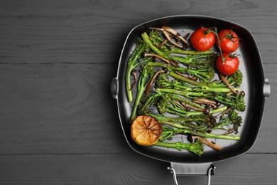 Grill pan with tasty cooked broccolini, mushrooms, tomatoes and lemon on grey wooden table, top view. Space for text