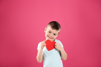 Portrait of boy with paper heart on color background