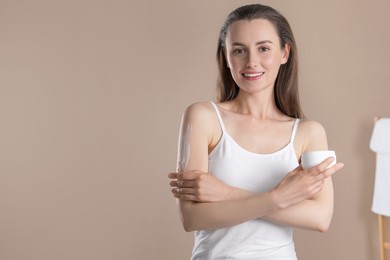 Photo of Happy woman applying body cream onto arm on beige background, space for text