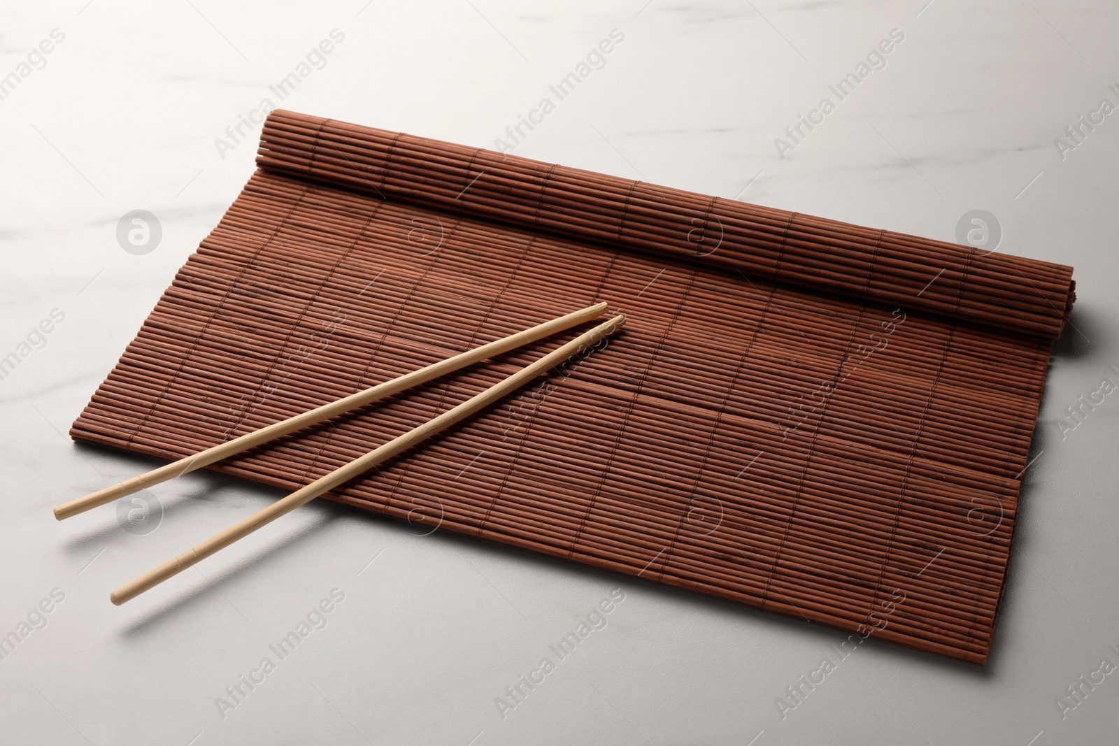 Photo of Rolled bamboo mat and chopsticks on white marble table