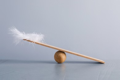 Photo of Wooden ball, small plank and feather on grey background. Balance concept