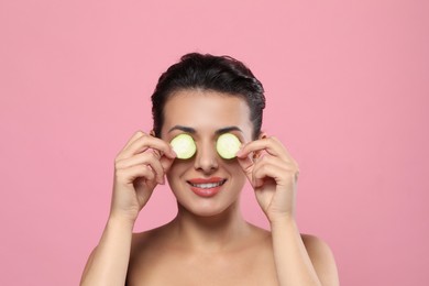 Photo of Woman covering eyes with cucumber slices on pink background. Skin care