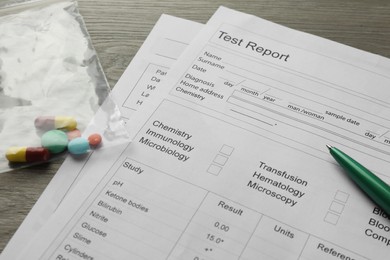 Photo of Drug test result form, pills and pen on wooden table, closeup