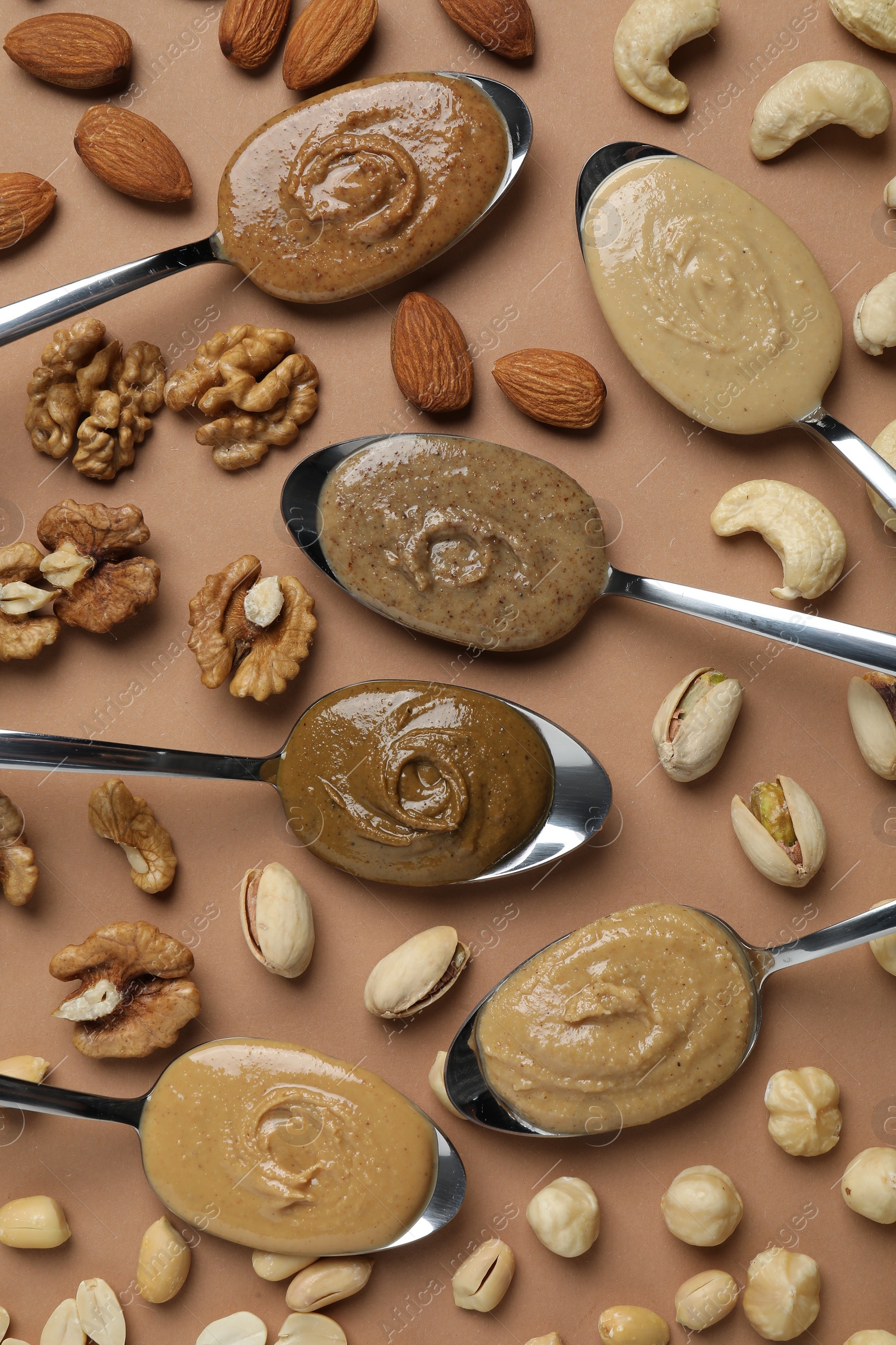 Photo of Tasty nut butters in spoons and raw nuts on light brown table, flat lay