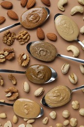 Tasty nut butters in spoons and raw nuts on light brown table, flat lay